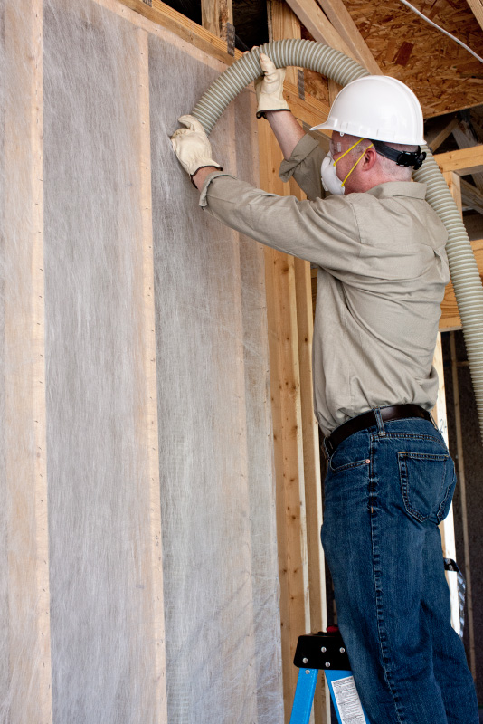 Male worker installing dense-packed cellulose insulation in a wall.