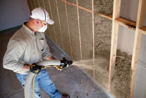 Male worker installing cellulose insulation in a wall.