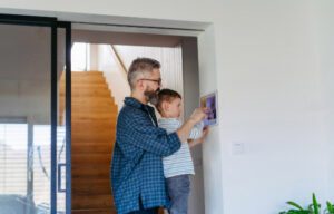 A father and his young child adjusting a smart thermostat on the wall to optimize home energy efficiency.