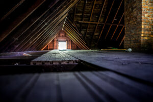 Old attic space with roof rafters and a window, shallow focus on floor.
